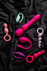 Collection of sex toys on a black sheet. Top view of various vibrators. 