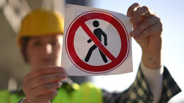 A construction worker shows a no pedestrian sign indicating restricted access in the construction zone