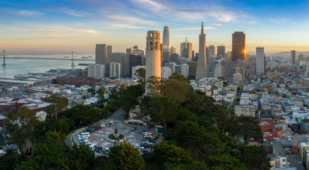 An aerial view of Coit Tower and the San Francisco skyline, including the Transamerica Pyramid, at sunset in California, USA. Tourists visit the landmark.