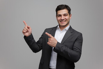Young businessman in a sleek suit exudes confidence while gesturing with enthusiasm against a minimalist gray backdrop