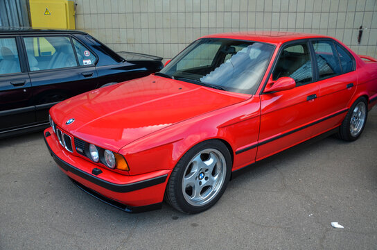 Brilliant red classic BMW E34 M5, showcasing its iconic sports sedan design. The car features multi-spoke silver alloy wheels and black trim accents