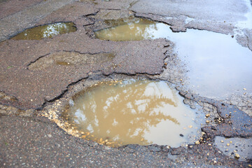 Wet potholes on asphalt road with reflections from rainwater