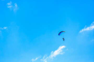Skydiver paragliding against bright blue sky with white clouds