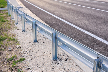 Close-up of metal highway guardrail along asphalt road in rural setting