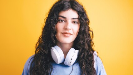 Young student posing with headphones on yellow background