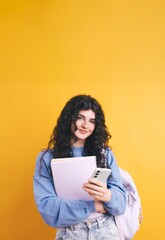 Smiling student using smartphone and holding notebook on yellow background