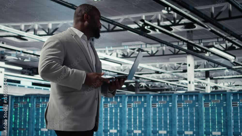 Poster admin walking in data center industrial platform analyzing infrastructure performance outputs on lap