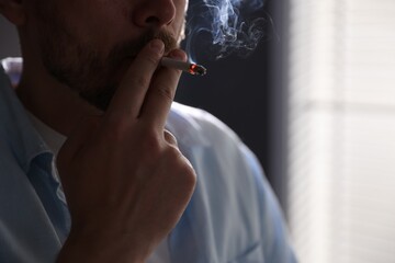Fototapeta premium Man smoking cigarette on blurred background, closeup