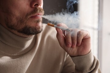 Man smoking cigarette near window indoors, closeup