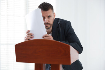 Fear of public speaking. Nervous man with microphone at lectern indoors