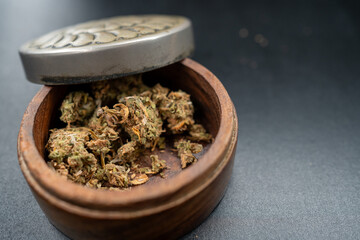 Wooden container with a metallic lid is partially open, revealing dried cannabis inside. The...
