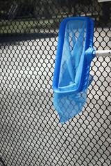 Swimming pool skimmer hanging on fence