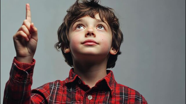 Curious boy looking up with dreamy eyes and smile on his face against gray background. 