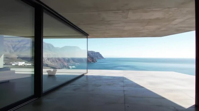 Contemporary oceanfront home with floor-to-ceiling glass walls overlooking a calm seascape and rocky coastline.

