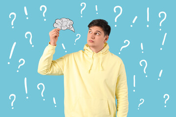 Young man holding speech bubble with question marks on blue background
