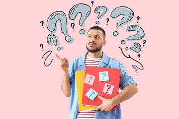 Portrait of thoughtful young man holding folders with question marks on pink background