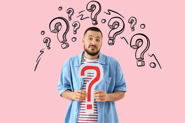 Portrait of confused young man with question mark on pink background