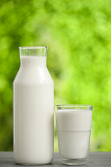 Glass and bottle of fresh milk on grey wooden table outdoors