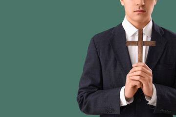 Young man with wooden cross praying on green background, closeup
