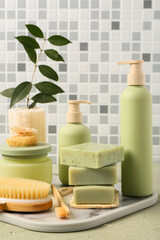 Tray with different cosmetic products and bath supplies on table against grey tile wall