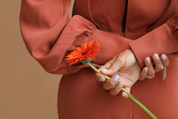 Young woman with beautiful manicure holding gerbera flower on color background, closeup