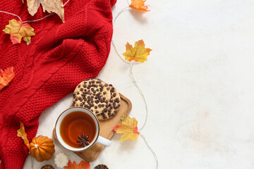 Composition with cup of tea, cookies, stylish sweater and autumn leaves on light background