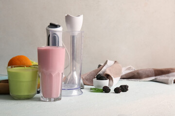Modern blender with glasses of smoothie, berries and fruits on light background
