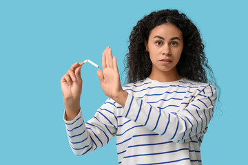 Young African-American woman rejecting broken cigarette on blue background. Stop smoking concept