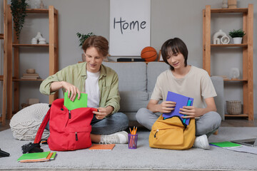 Male students putting copybooks into backpacks at home
