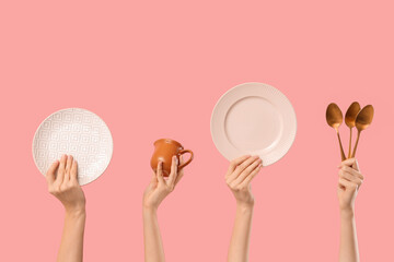 Female hands with plates, jug and spoons on pink background