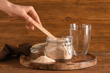 Female hand and jar with psyllium husk powder with glass of water on wooden background
