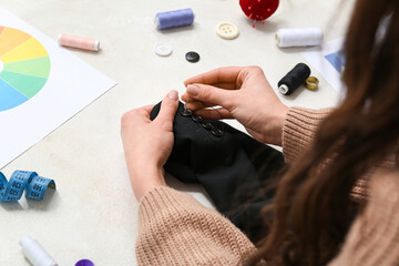 Woman sewing button on black coat's sleeve at white table, closeup