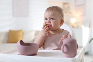 Cute little baby eating on feeding chair at home