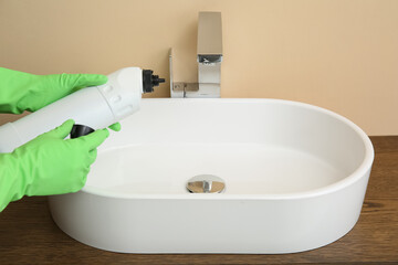 Woman in rubber gloves cleaning clogged drain with liquid cleaner in bathroom