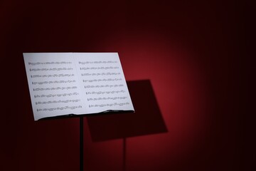 Note stand with music sheets on dark red background, space for text