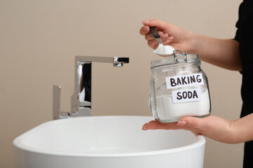Woman with jar of baking soda near clogged sink, closeup