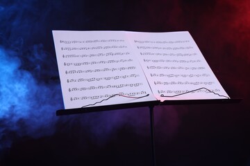Stand with music sheets on dark background with smoke, closeup