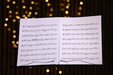 Note stand with music sheets against blurred lights, closeup. Bokeh effect