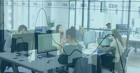 Typing center figure wearing dark top, using desk in open plan office, with monitors and headsets