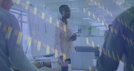 Presenting woman holding tablet while sharing financial charts in office meeting, with laptop