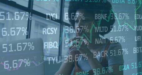 Analyzing financial data overlays on laptop screen at desk in office, woman holding pen to lips