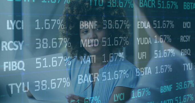 Holding notebook and pen, woman in blue blouse analyzing data on office glass wall, with laptop