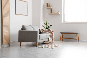Interior of light living room with grey sofa, soft bench and bookshelves