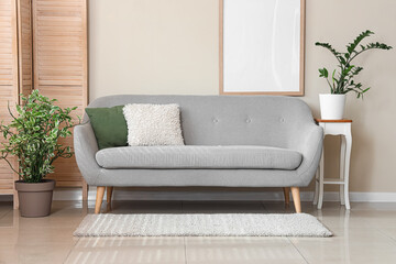 Interior of light living room with grey sofa, blank frame and folding screen