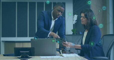 Professionals wearing suits pointing at tablet beside laptop on meeting table, with documents