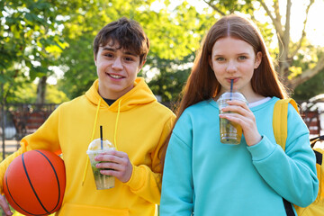 Teenage girl and boy with drinks and basketball in park