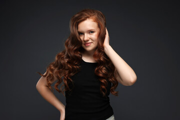 Fototapeta premium Portrait of beautiful teenage girl with healthy wavy hair on dark grey background