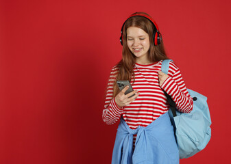 Teenage girl with smartphone listening to music on red background. Space for text
