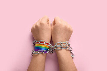 Hands with LGBT ribbon and chains on pink background. Concept of oppression