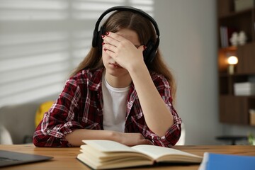 Stressed teenage girl studying at desk indoors